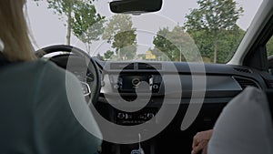 Two women driving car on narrow road with deciduous trees on both sides approaching to small European town. Back view