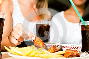 Two women eating chicken wings and drinking soda