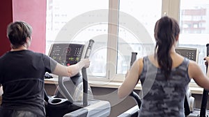 Two women are engaged on exercise machines in the gym. Trenerovka of women. Girls do exercises at a window. Sports. Gym