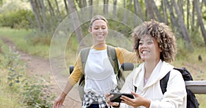 Two women enjoy a hike in a wooded area, one with a phone in hand