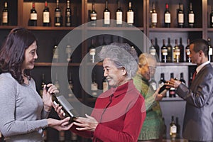 Two women in the foreground buying and discussing wine, two men in the background