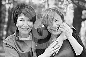 Two women friends 60s and 40s years hugging and walking in park