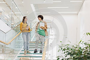 two women friends of colleagues walk up glass steps in coworking office. Female students discuss work project