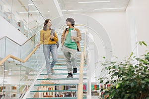 two women friends of colleagues walk up glass steps in coworking office. Female students discuss work project