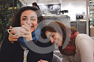 Two women friends enjoying a joke and a chat and a cup of coffee or tea, laughing and smiling in a cafe