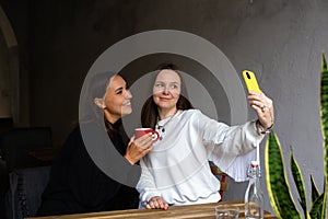 Two women friends have fun outdoors in cafe and take a selfie on a smartphone