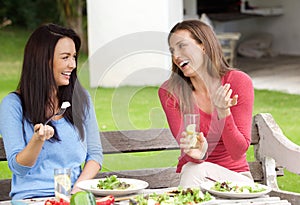 Two women friends sitting outside in garden having lunch