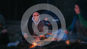 Two women fry sausages on a fire. Family camping at night.