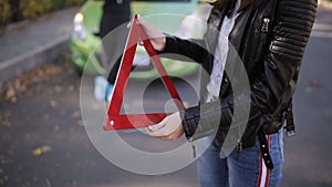 Two women on a green car struck the wheel and install the emergency sign on the road.