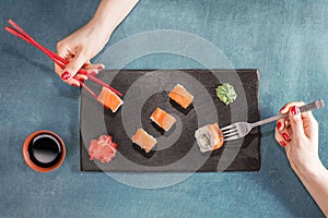 Two women hands with chopsticks and fork.