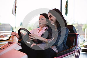 Two women having a lot of fun in the amusement park, driving bumper cars