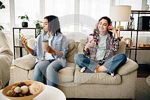 Two women in headphones leisures on sofa