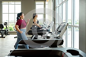 Two women with a heavier build running on treadmills in a modern gym