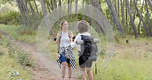 Two women are hiking on a forest trail, one with a plaid shirt tied around her waist