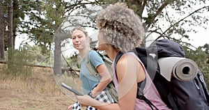 Two women are hiking in a wooded area, one holding a smartphone