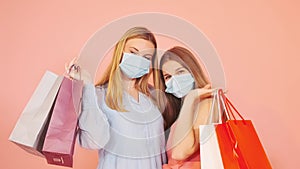Two women holding shopping bags and having fun together on a pink background