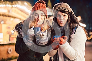 Two women with hot mulled wine in front of Christmas market stand