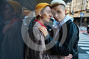 Two women hugging each other on city street near modern buildings