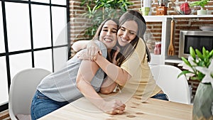 Two women hugging each other sitting on table at dinning room