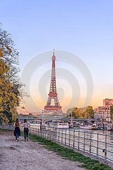 Two women jogging by Seine river on island iles aux cygnes in autumn with sunset view of Eiffel tower