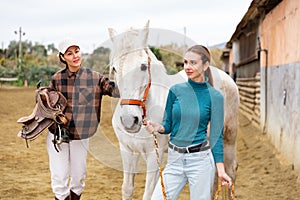 Two women jokey preparing horse for riding in paddock