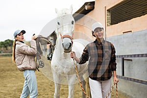 Two women jokey preparing horse for riding in paddock
