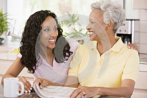 Two women in kitchen with newspaper and coffee