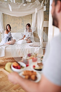 Two women laughing surprised by a guy brining them breakfast in bed. lesbian, bisexual, threesome concept photo