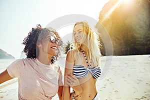 Two women laughing while walking together along a sandy beach