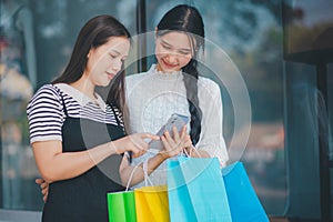 Two women are looking at a cell phone while holding shopping bags
