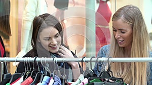 Two Women Looking At Clothes On Rail In Shopping Mall