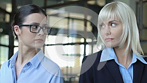 Two women looking different sides, competing at work, blond and brunette rivalry