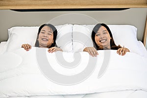 Two Women Lying Down on White Bed, Smiling and Enjoying Time Together