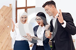 Two women and a man are drinking coffee and watching something on the laptop screen.