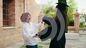 Two women mother and daughter celebrating graduation dancing at campus university