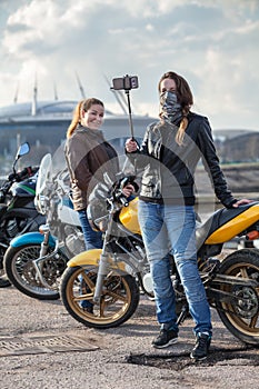 Two women motorcyclists making photo with selfie stick and front camera of cellular