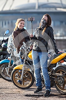 Two women motorcyclists making photo with selfie stick and front camera of cellular