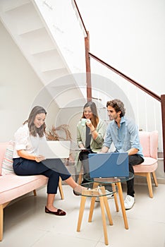 Two women and one man businessmen working informally on their computers in their office chairs