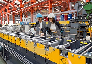 Two women operate machinery in a factory, wearing safety gear and focused on their task