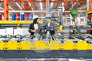 Two women operate machinery in a factory, wearing safety gear and focused on their task