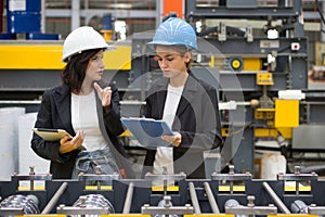 Two women operate machinery in a factory, wearing safety gear and focused on their task