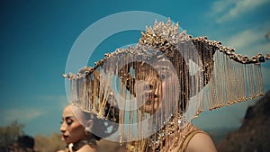 Two women in ornate headpieces with a blurry blue sky background
