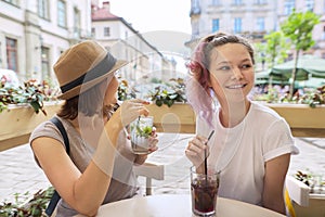 Two women in outdoor cafe talking, drinking summer ice cold drinks