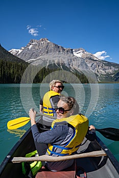 Two women paddling on a canoe turn around and smile, while boating on Emerald Lake in Canada