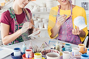 Two women painting own ceramic tableware in DIY workshop