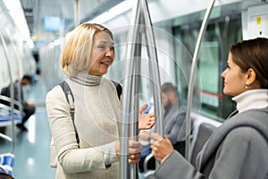 Two women passengers talking in subway car on way to work