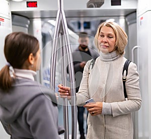 Two women passengers talking in subway car on way to work