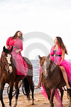 two women in pink dresses riding horses along the beach at sunset