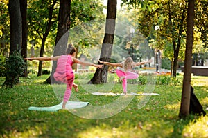 Two women in the pink sportsuit practice yoga in the park