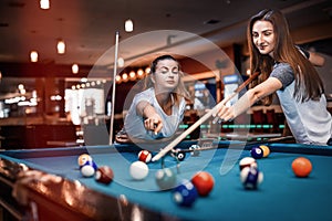 Two women playing billiard using cue rack